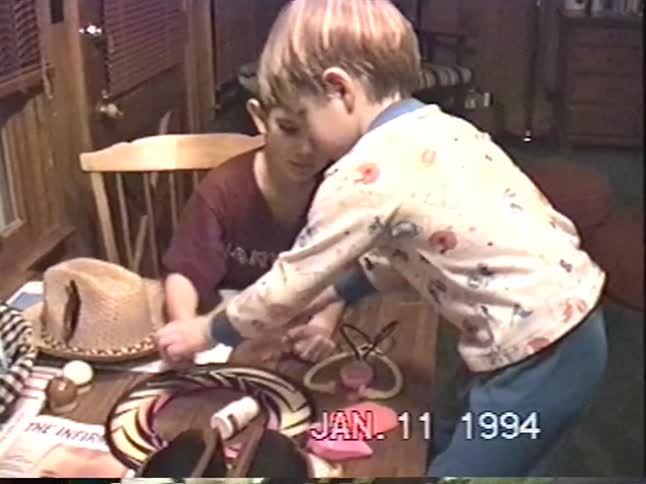 Two young brothers play with toys at a table in their pajamas in a vintage home video from 1994