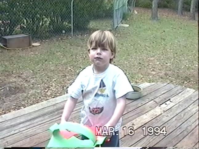 A cute little boy in a handmade paper leprechaun costume for St. Patrick's Day smiles and makes faces in this 1994 home video