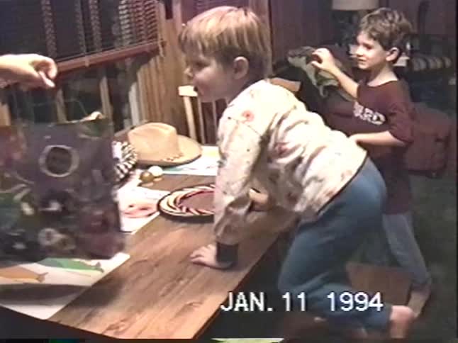 A nostalgic VHS home video from 1994 captures the joy of children opening presents at a family gathering