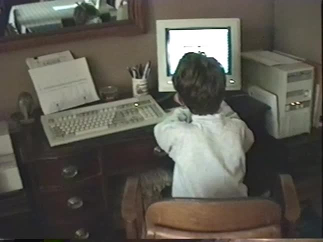 Vintage home video of a family relaxing indoors with a black dog and a young boy using an old desktop computer