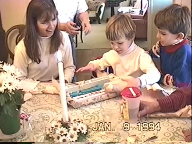 Vintage VHS footage from 1994 shows a happy family celebrating as a young boy unwraps his birthday present at the dining table