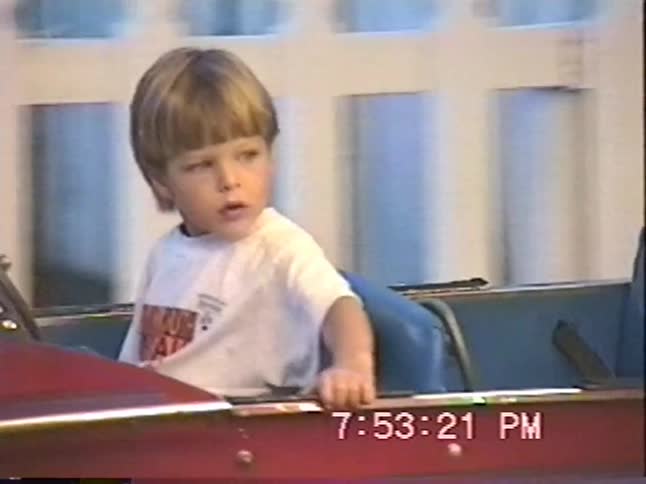 Vintage home video footage shows a little boy riding a classic car carousel at an amusement park