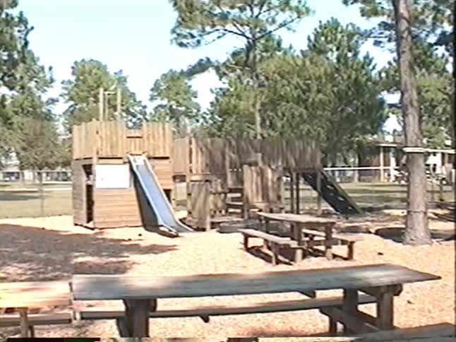 A father helps his young child onto a rope swing at a rustic outdoor playground in this vintage home movie