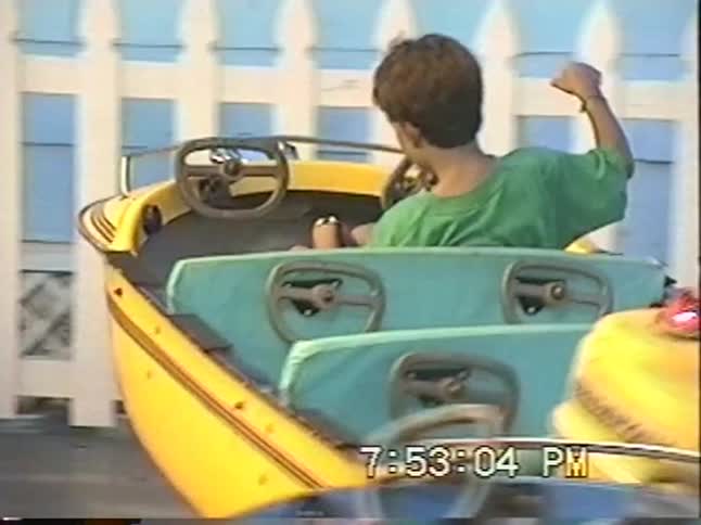 A young boy in a green shirt enjoys a vintage spinning car ride at an amusement park