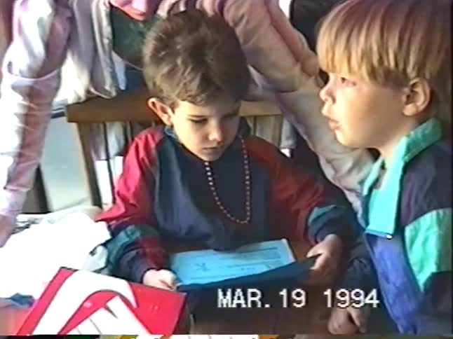 Vintage home video from 1994 shows two young brothers in colorful windbreakers looking at papers with their father