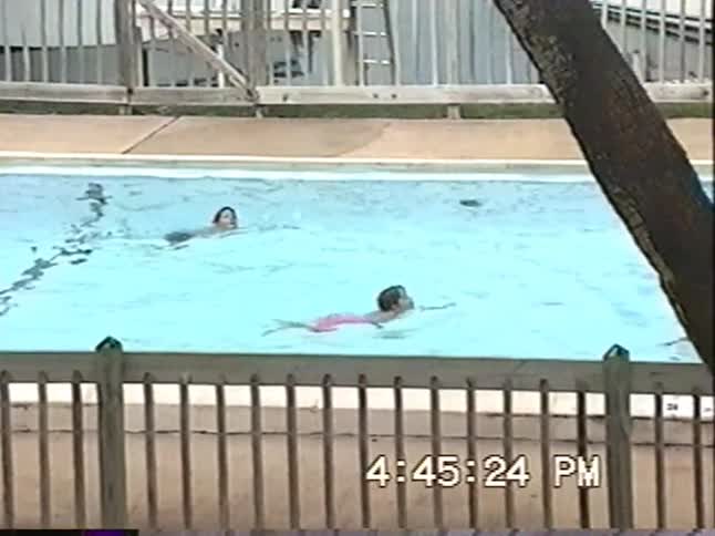 Archival home video footage shows two young children swimming in a community pool on a bright summer day