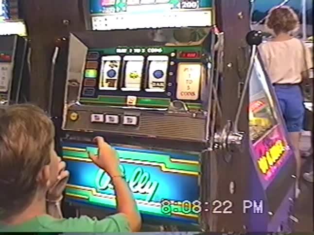 Retro VHS footage shows a young boy playing a classic slot machine in a casino or arcade