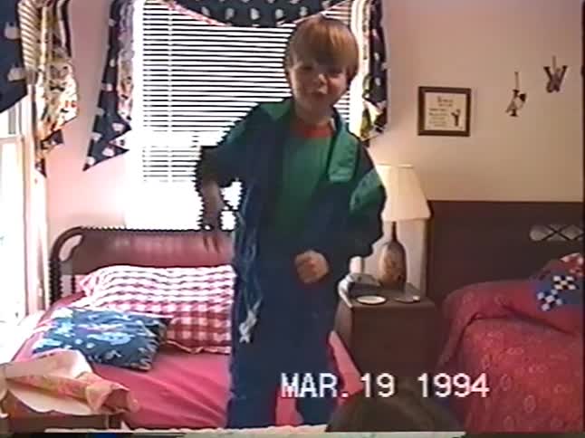 Vintage home video from 1994 shows a mother helping her son put on his colorful windbreaker while another child plays in the background