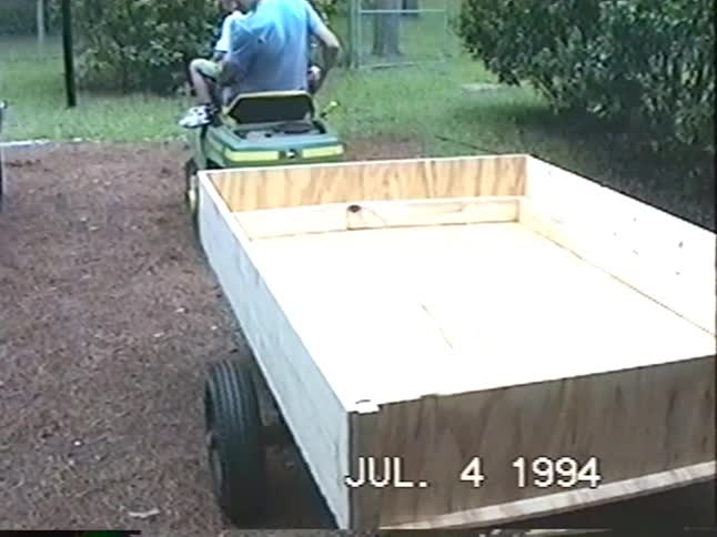 Vintage 1994 home video shows a father and son hitching a homemade wooden trailer to a lawnmower tractor in their backyard