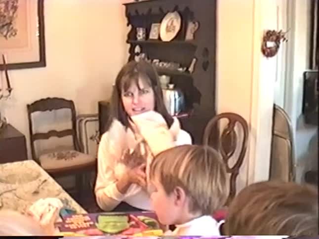 Two young boys excitedly unwrap a "Big Frank" toy for a birthday present while the family watches