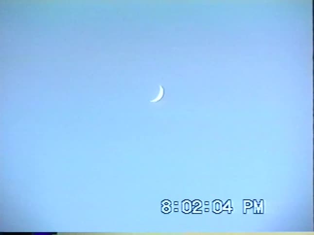 A vintage home video captures a small carnival Ferris wheel before panning up to the crescent moon in the evening sky