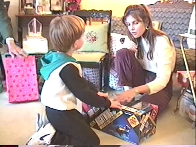A mother and her young son excitedly examine a large new remote control car toy in its box on Christmas morning