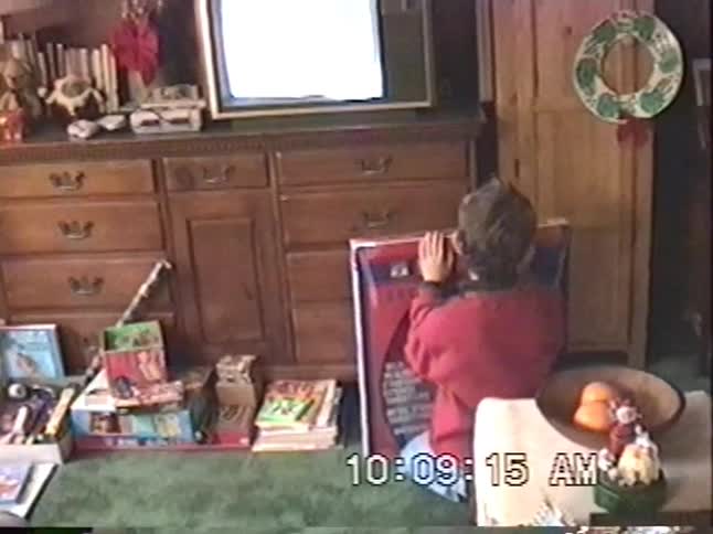 A man talks on the phone while his kids enjoy their new presents on Christmas morning in this vintage home video