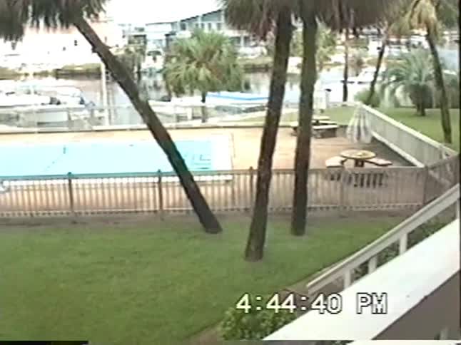 Authentic 1990s VHS footage shows two young children playing and swimming in an outdoor pool near a waterway with boats
