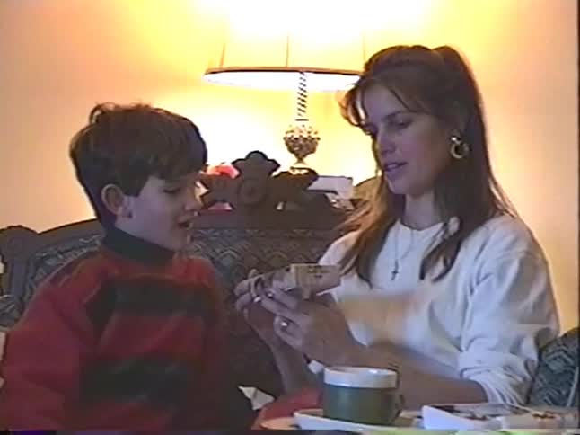 A mother and her young son share a happy moment opening presents together in their living room in this vintage home video