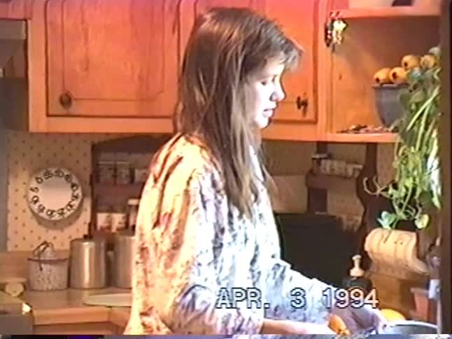 A woman in pajamas washes fruit in a colander in her country-style kitchen in this authentic 1994 home video