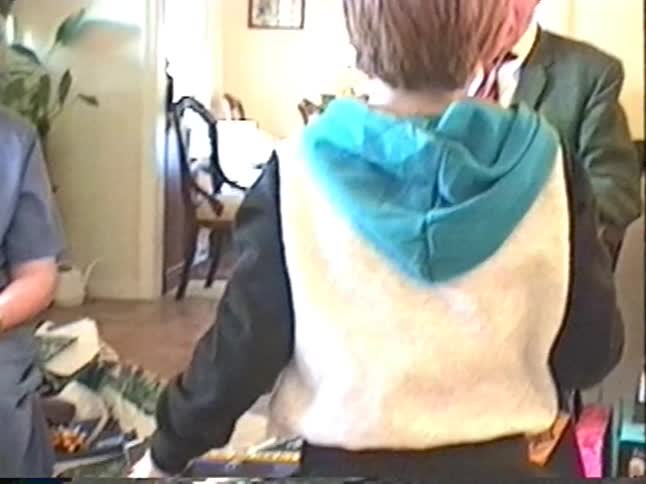 An excited young boy opens a large Christmas gift as his proud grandparents look on in a 90s home video