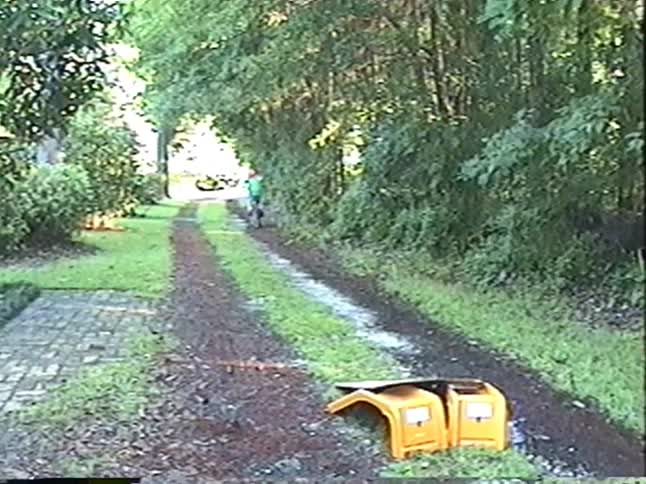 Nostalgic VHS footage shows a father teaching his two young children to ride their bikes on a rural dirt path, with the son excitedly tackling a small ramp