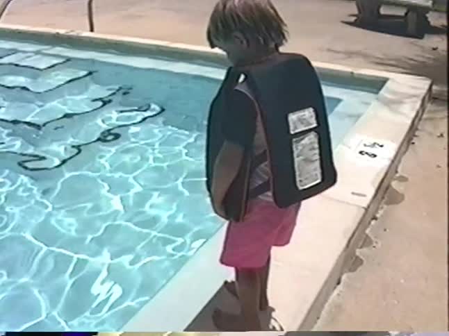 A happy young boy wearing a life vest gets excited to swim in the pool with his mother on a sunny day