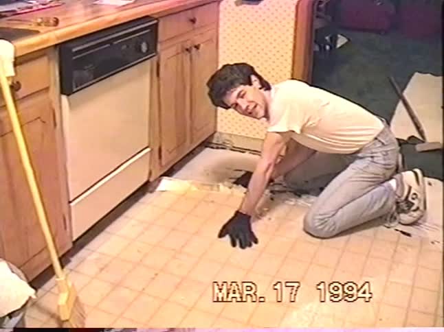 Vintage 1994 footage of a man opening a wine bottle before starting a DIY project to remove the kitchen floor tiles