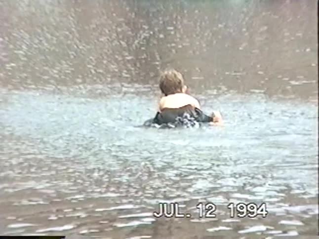 A vintage 1990s home video captures the joy of children swimming and playing in a flooded motel parking lot after a storm