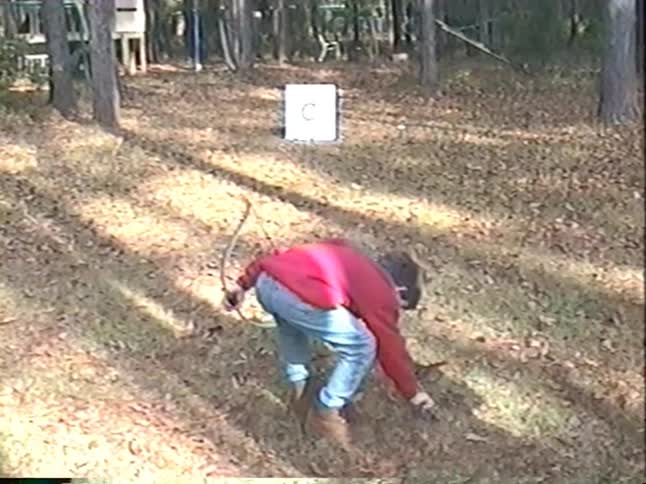 Vintage VHS footage of a young boy in a red jacket practicing archery in a wooded backyard