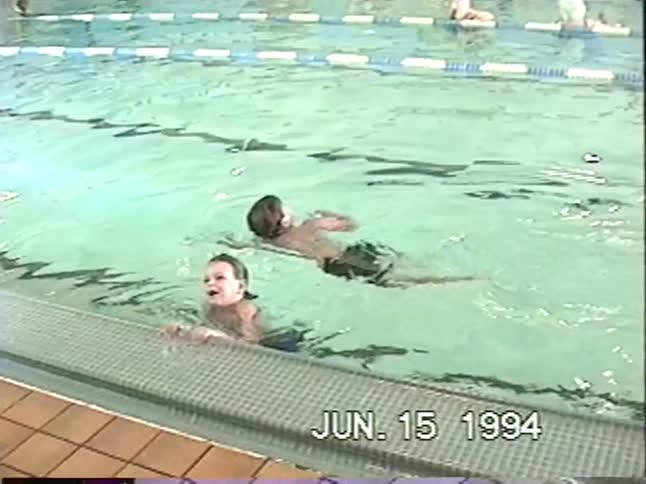 Young children practice swimming during a lesson at an indoor community pool in this vintage 1994 VHS home movie