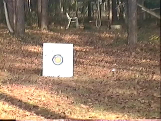 A vintage home video shows a young boy practicing archery in the woods, hitting the target with his bow and arrow