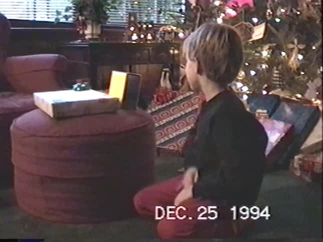 A young boy sits by the Christmas tree and opens his presents on Christmas morning in 1994