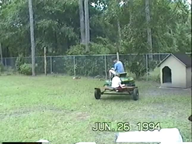 A wholesome 1994 home video shows a father and his children playing outside, riding bikes over a ramp, and enjoying a lawnmower trailer ride
