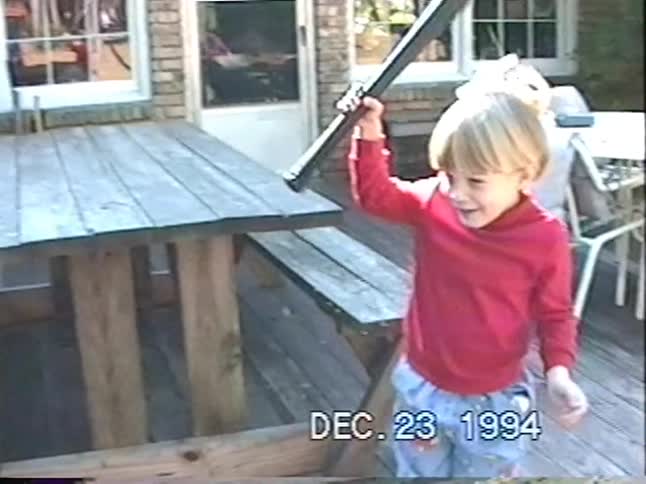 Nostalgic home video from 1994 shows two young boys playfully posing with toy baseball bats on a backyard deck