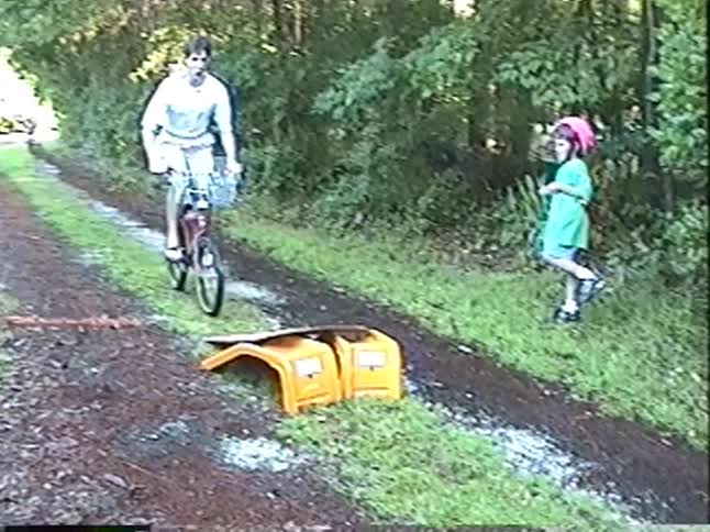 Nostalgic VHS footage of a father and two young children riding bikes and doing jumps on a makeshift ramp in their backyard