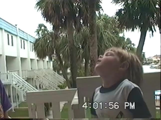 Slow motion VHS footage from the 90s shows two young boys playing with a colorful bubble gun on a motel balcony
