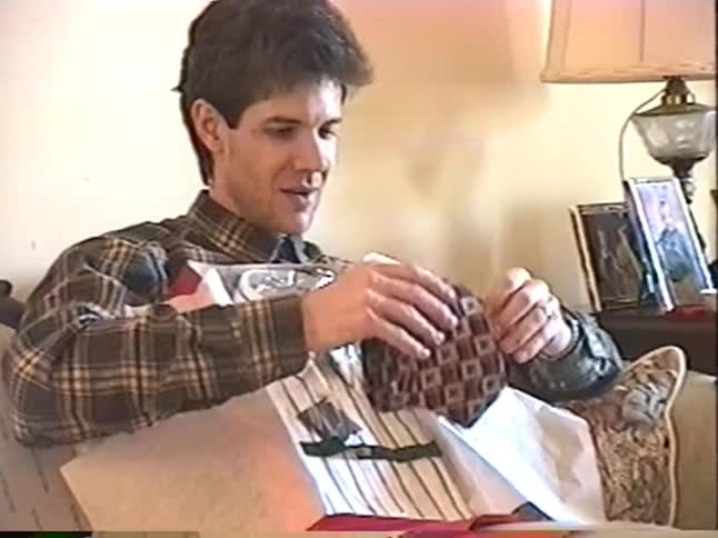 Excited young boys watch as their father opens a Christmas present containing a new shirt and tie