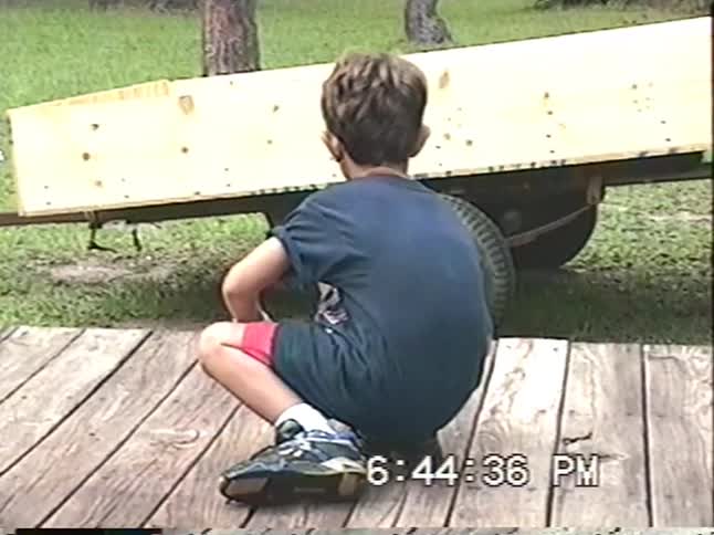 Vintage home video of two young boys playing with sparklers and lighting a smoke bomb that explodes on a wooden deck