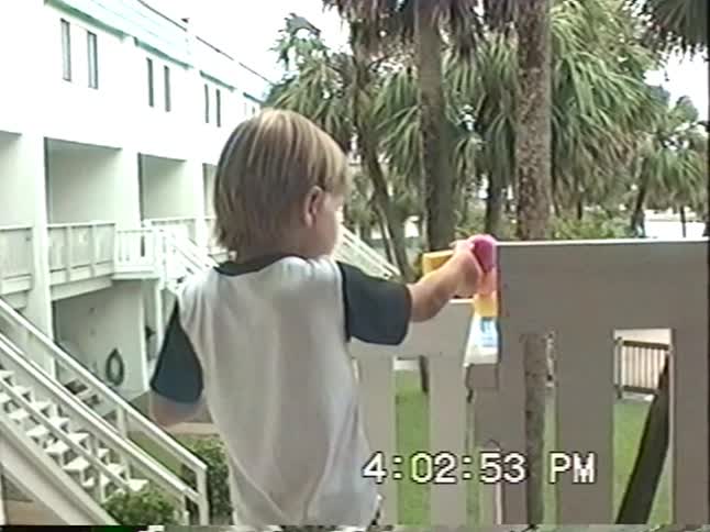 Vintage VHS footage from 1994 shows two young boys playing with bubbles and toys on a tropical hotel balcony overlooking a pool and marina