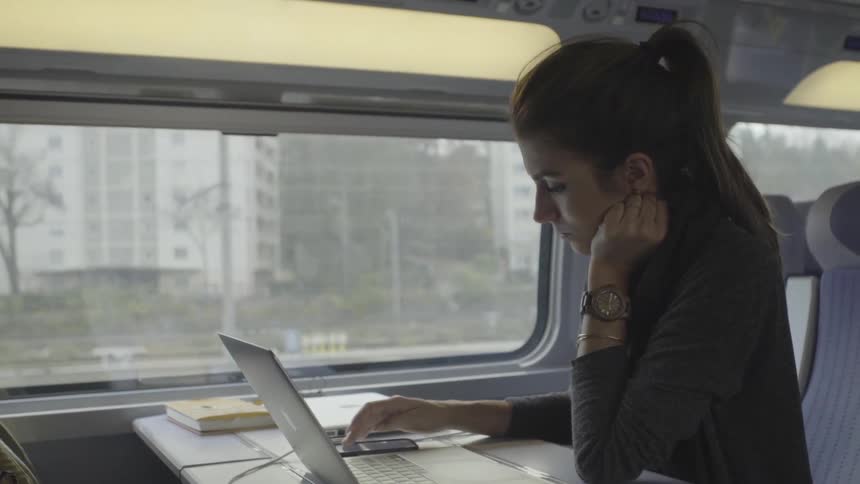 Woman riding on a train looking at a laptop