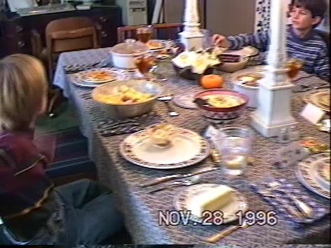 A young boy smiles while sitting at a beautifully set dining table for Thanksgiving dinner in a vintage home video from 1996