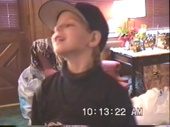 A nostalgic home video shows a young boy in a baseball cap happily talking with his family on Christmas morning