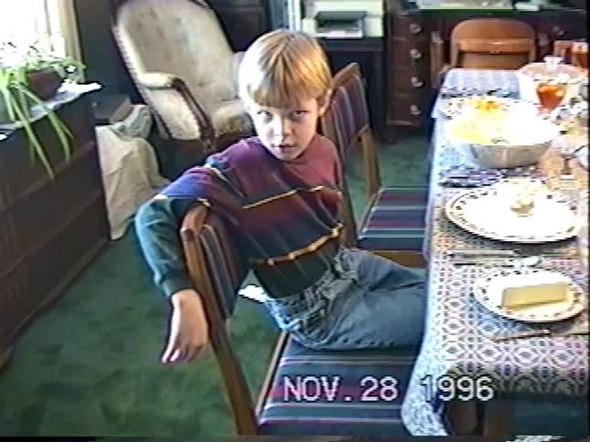A young boy smiles and talks at the dinner table on Thanksgiving day in a home video from 1996