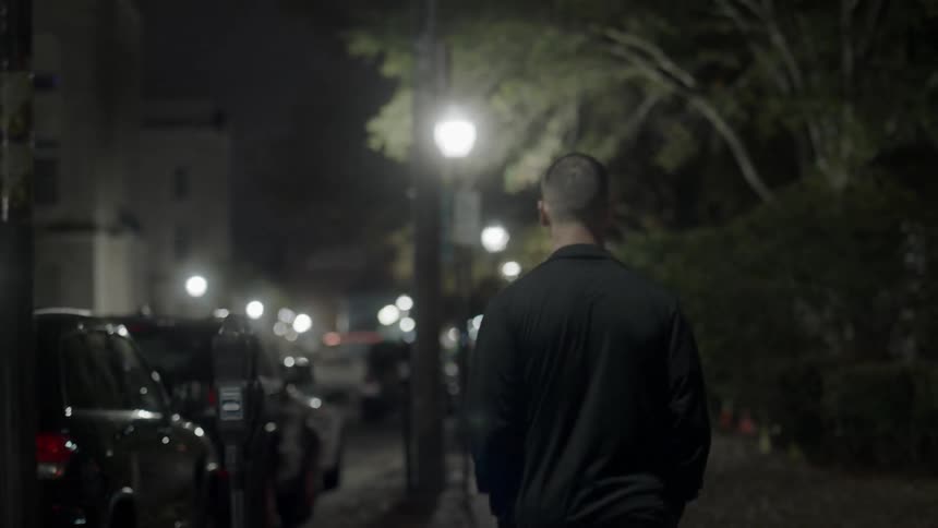 A man walks down a city sidewalk at night