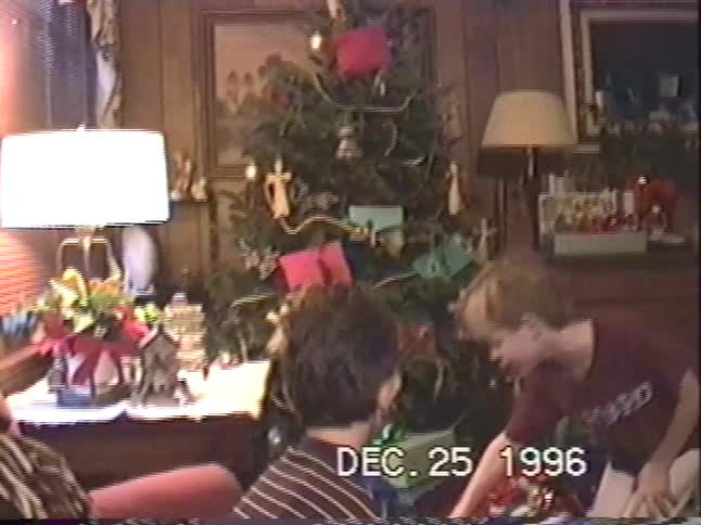 Two young boys excitedly gather around a decorated Christmas tree to open presents on Christmas morning in 1996