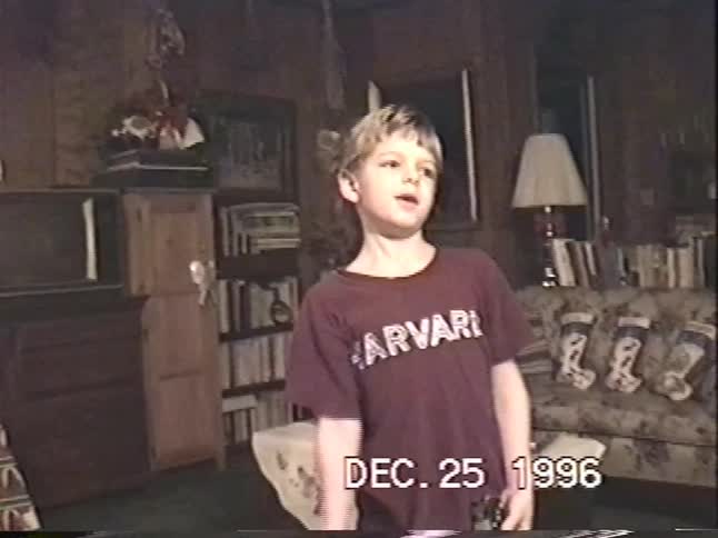 A young boy in a Harvard shirt excitedly opens his presents on Christmas morning in this nostalgic 1996 home video