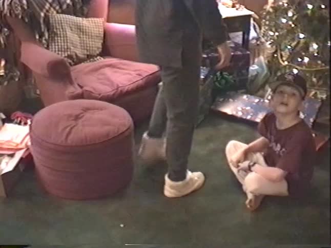 Vintage VHS footage captures a young boy and his mother celebrating Christmas morning in a cozy living room