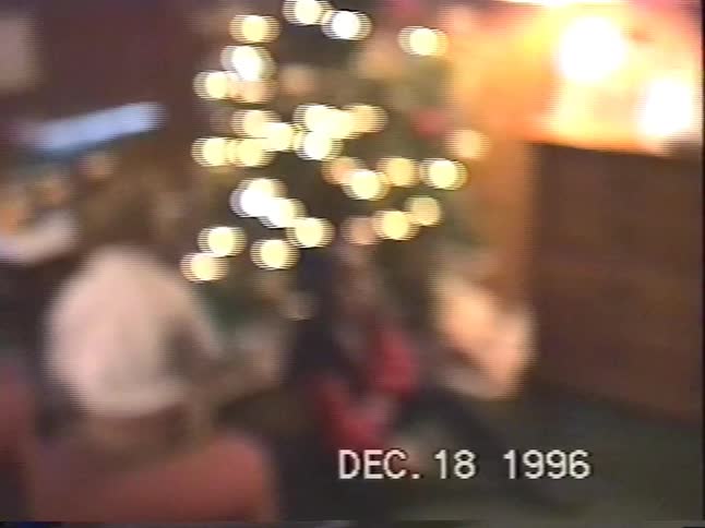 A vintage home video from 1996 shows two young children and their dog sitting by a brightly lit Christmas tree
