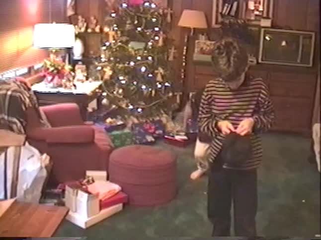 Two young brothers shout with joy as they open new baseball caps for Christmas in front of the tree in this nostalgic home video