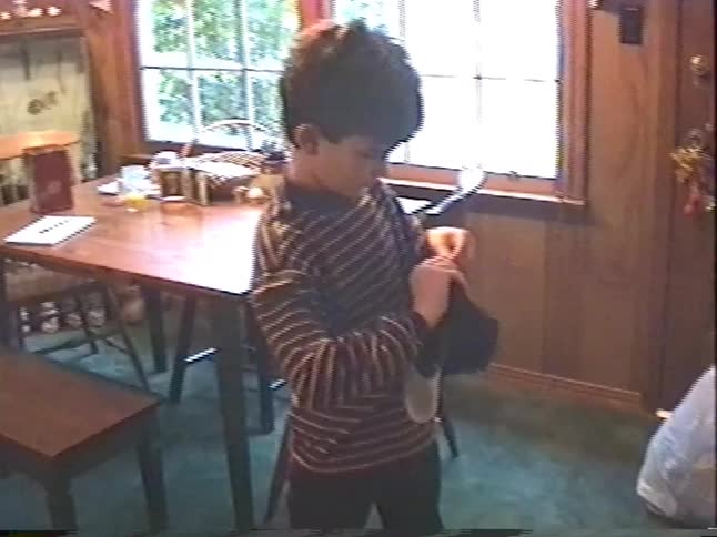 A young boy excitedly tries on and adjusts his new baseball cap in a vintage home video from Christmas
