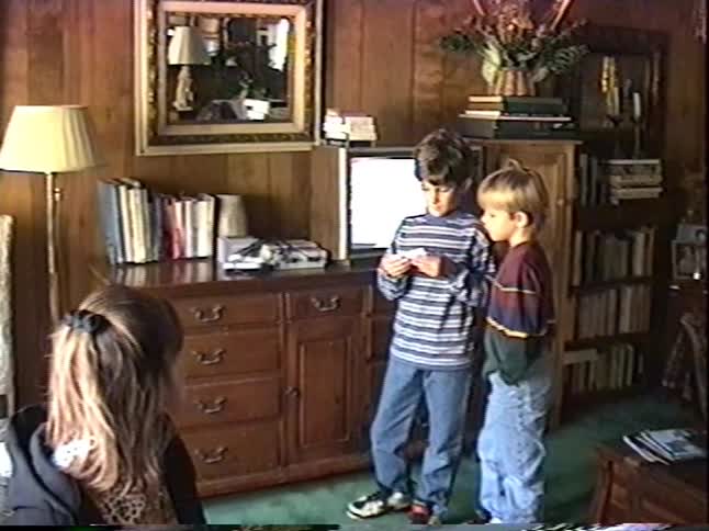 Vintage home video of a mother and her sons in a 1990s living room as one gets a new SNES video game