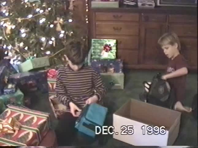 Vintage VHS footage from Christmas 1996 shows two excited young boys opening their presents by the Christmas tree
