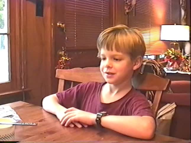 Young boy sits at a wooden dining table and proudly shows his digital wristwatch in a warm home interior